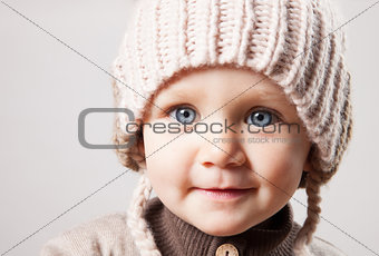 Portrait of a cute baby girl in a huge brown knitted hat. Isolated on white background.