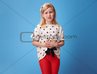 sad modern child in red pants on blue with abdominal pain