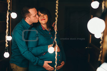 Man hugs his pregnant woman on a lamps background