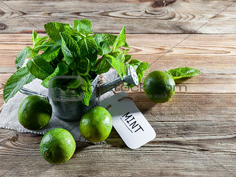 Fresh mint leaves in a vintage watering can and green limes on a wooden background.