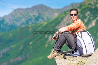 active tourist sits on a rock in the mountains with a backpack, 