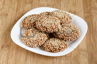 Oatmeal cookies with sesame seeds in a white dish on a wooden ba