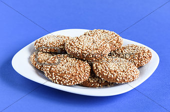 Oatmeal cookies with sesame seeds in a white dish on a violet ba