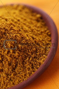 pile of bright Madras Curry Powder in teracotta dish on orange b