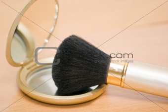 Brush for makeup reflected in mirror on wooden table
