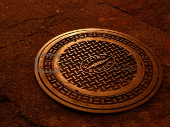 And electric service manhole cover shinning in soft copper tone under the street lights at night